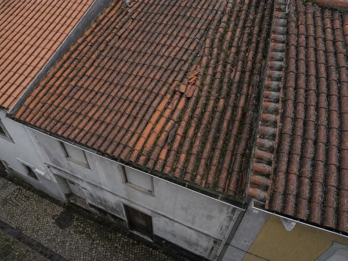 Vista de drone de um telhado antigo e inclinado entre casas vizinhas, numa rua estreita
