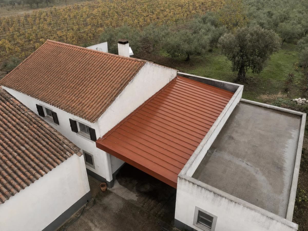 Vista aérea de uma propriedade no Ribatejo com três telhados: telha sobre madeira na casa, painel sanduíche no anexo e laje plana na ampliação